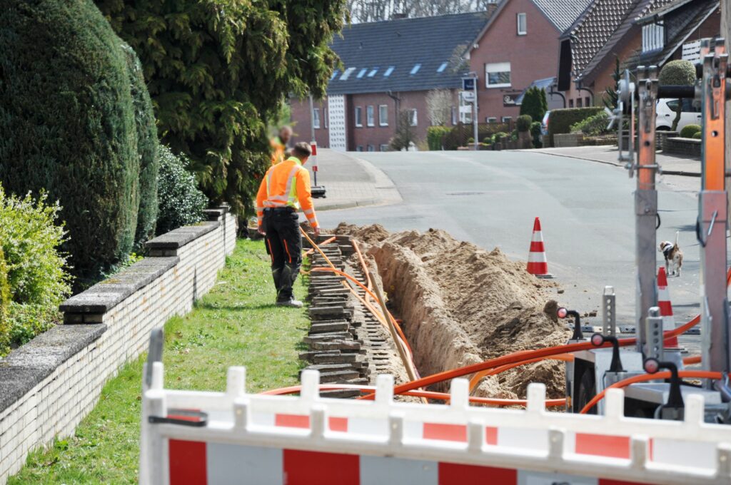 Zwei Bauarbeiter arbeiten auf einer Baustelle, auf der Glasfaser in einem Wohngebiet verlegt wird.