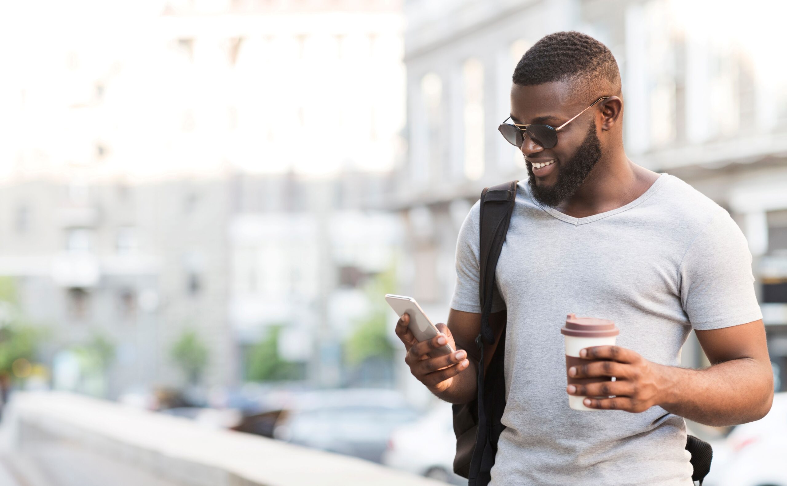 Ein Mann hält in der einen Hand sein Handy und in der anderen einen Kaffeebecher.