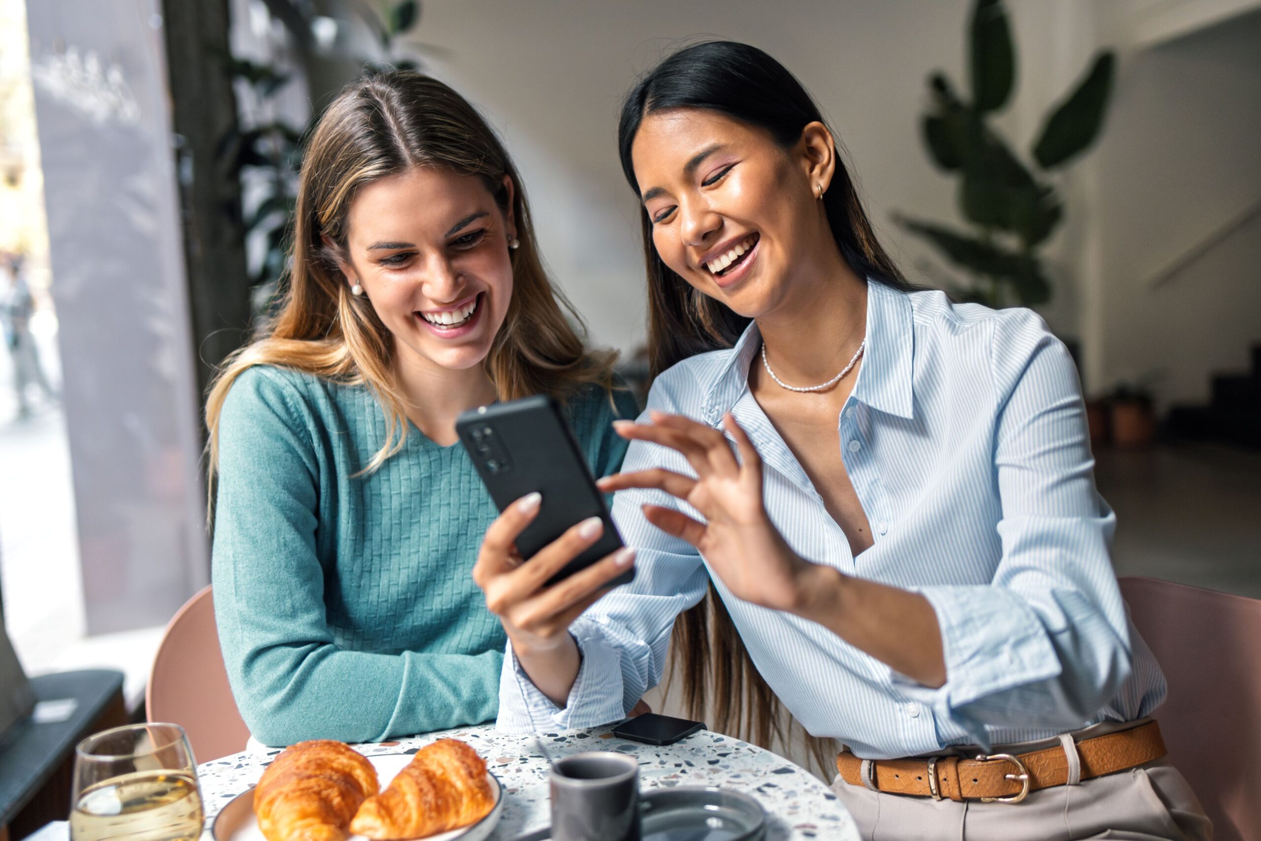Zwei Frauen sitzen in einem Café und schauen gemeinsam auf ein Handy.