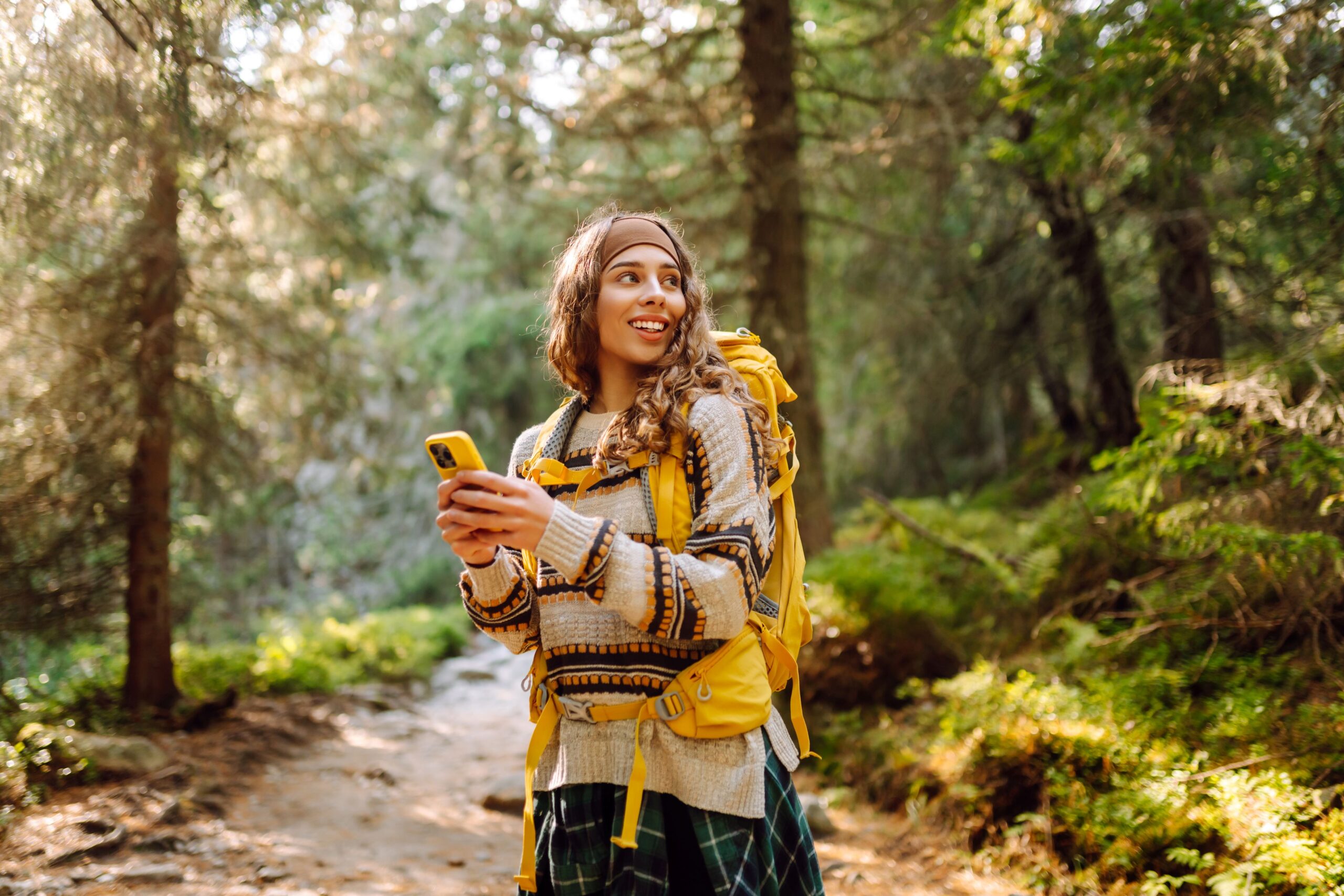 Eine Frau wandert in einem Wald und hält ihr Handy in der Hand.
